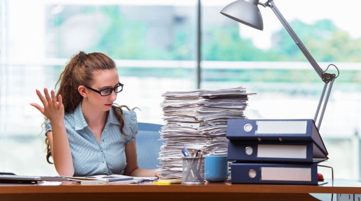 Woman Sitting At A Desk With A Stack Of Papers